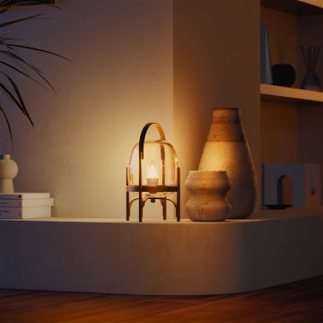 Eine Glas-Tischleuchte, ausgestattet mit einer smarten Philips Hue Lampe, strahlt ein warmes Glühen auf ein modernes Regal mit dekorativen Vasen und Büchern.