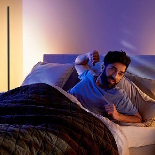Een man ligt in bed en wordt rustig wakker bij het zachte warmwitte licht van een Signe vloerlamp.