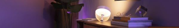 Philips Hue table lamp casting a warm glow on a side table beside a decorative plant.