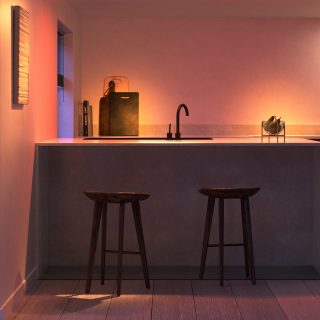 Et moderne køkken oplyst af varm Philips Hue intelligent belysning, hvilket skaber et indbydende rum til madlavning og spisning.