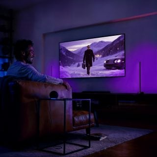 Persona viendo la televisión en un salón con luces inteligentes Philips Hue sincronizadas con el contenido de la pantalla para una experiencia de entretenimiento inmersiva.