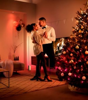 A couple celebrate the festive season in their living room with Philips Hue holiday lighting and tree lighting that fills their space with shades of red and white smart light.