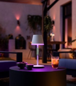 A Hue Go portable table lamp lights up a patio table with purple tones of smart light.