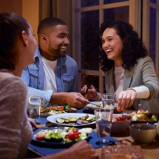 Tre amici mangiano insieme a casa con luci intelligenti dai toni caldi.