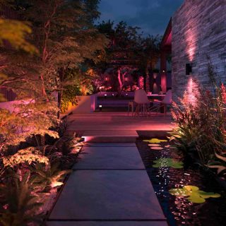 Una parete del giardino illuminata con applique e faretti impostati sulle tonalità rosa e arancione.