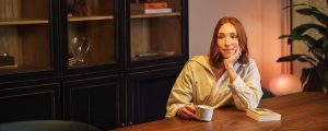 따뜻하고 밝은 Philips Hue 스마트 조명으로 아늑하게 빛나는 거실에서 식탁에 앉아 휴식을 즐기는 사람입니다.