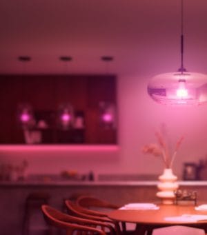 Een eettafel verlicht door een hanglamp die slimme verlichting in zachtroze tinten geeft.