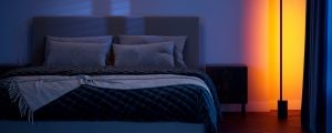 A Philips Hue Signe gradient floor lamp available in the Black Friday lighting sale washes a bedside in yellow and pink tones of smart light.