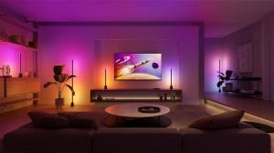Hue Play golv- och bordslampor placerade runt TV-området i vardagsrummet lyser med färggradienter i rosa, blått och gult ljus som speglar TV:ns skärminnehåll.