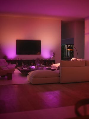 A TV mounted on a living room wall washed in surround wall washing lighting in pink and red tones of smart light.