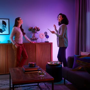 Två kvinnor som njuter av smart belysning i ett vardagsrum och styr belysningen med Hue-appen.