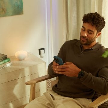 En mand styrer sin dørklokke, sin Chime og sine Philips Hue pærer i Hue appen på sin smartphone. 