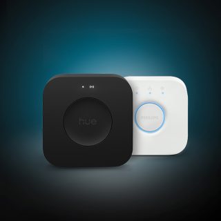 Hue Bridge Pro og Hue Bridge intelligente lysstyringssystemer til hjemmet. En person, der styrer Philips Hue intelligent belysning ved hjælp af Hue appen på en smartphone. En hvid Philips Hue Smart button placeret på et bord ved siden af en bærbar computer.