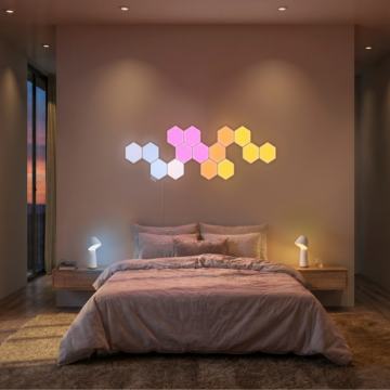 Modulare Nanoleaf Hexagon-Wandleuchten sind über einem Bett montiert, und Philips Hue Nachttischlampen erstrahlen dank intelligenter Beleuchtung in Rosa-, Orange, Gelb- und Weißtönen.