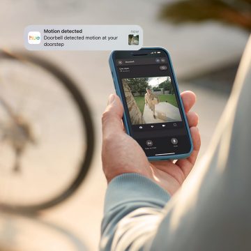 Eine Person, die sich an einem anderen Ort als ihrem Zuhause befindet, beobachtet ihre Eingangstür mit einer Hue Secure Video-Türklingel über die Hue App. 