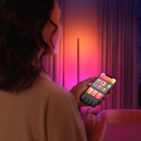 Ein mobiles Gerät mit der Hue App in der Hand einer Frau, die die Beleuchtung in einem modernen Wohnzimmer steuert.
