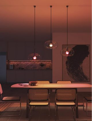 Drei smarte Hue Essential Lampen, eingesetzt in Pendelleuchten mit Glasschirmen, beleuchten einen Tisch mit pinkem und warmweißem Licht. 