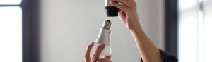 Hände einer Person, die eine weiße LED-Lampe in eine Deckenfassung einschrauben, wobei der Fokus auf der Verbindung zwischen Lampe und Sockel liegt.