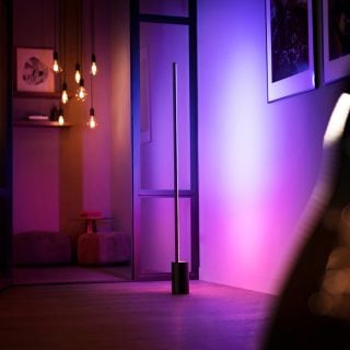 Eine Philips Hue Signe Gradient Stehleuchte taucht eine Wand in ein sanftes, pinkes und violettes smartes Licht.