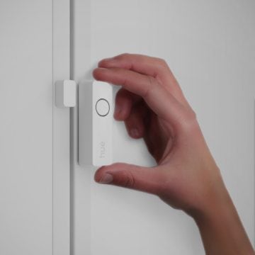 Eine Hand, die einen Hue Secure Kontaktsensor an einem Fensterrahmen anbringt