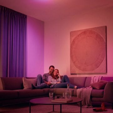 Ein Paar entspannt sich auf einem Sofa, umgeben von sanftem rosa und violettem, smartem Licht.