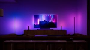 A living room entertainment setup with Philips Hue Play light bars and Play lamps either side of a TV and synced with the screen to create purple and pink wall washing effects. 