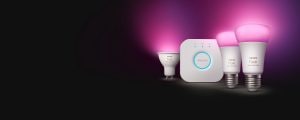 White and color smart bulbs with rounded shape and silver base, emitting pink light, shown beside a compact white hub.