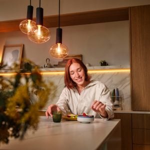 A woman eating at a table with Hue lights above her and a strip light behind her.