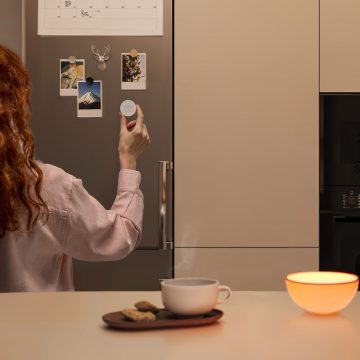 Woman placing a Hue smart button (latest model) onto the refrigerator with its magnetic mount