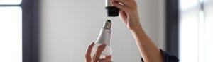 Person's hands installing a white LED light bulb into a ceiling socket, focusing on the bulb and socket connection.