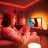 A woman gaming on her TV with an immersive entertainment lighting set-up glowing in red, orange and white smart light. 