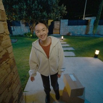 A girl viewed through a front door camera delivering packages to a home.