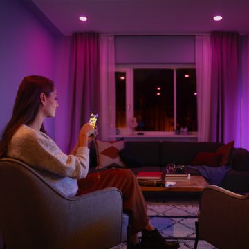 A woman sits on a sofa controlling her Hue smart lights with the Hue app.
