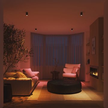 A living room space lit in warm tones of pink and white smart light.
