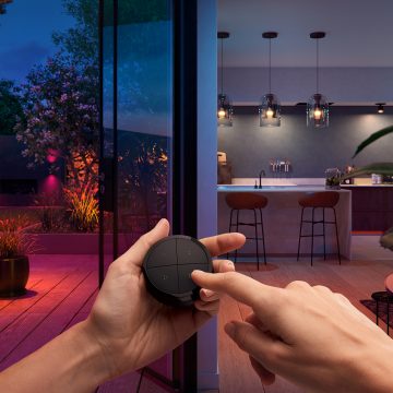 Hands holding a Tap dial switch, controlling the smart lights in a kitchen and garden simultaneously