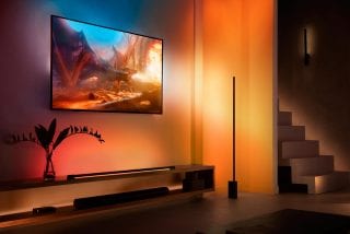 A Signe gradient floor lamps placed next to a TV entertainment lighting set-up glowing in orange tones of smart light. 