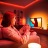 A woman gaming on her TV with an immersive entertainment lighting set-up glowing in red, orange and white smart light. 