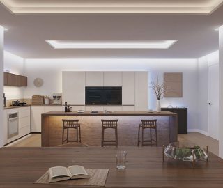 A kitchen lit with bright white indirect light from strip lights concealed under countertops and ceiling and wall coves to create a wall washing effect. 