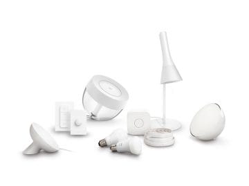 A collection of smart lighting and sensor devices in white, including bulbs, remotes, lamps, and motion sensors, arranged together.