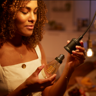 Person installing a filament-style smart bulb into a pendant socket in a warmly lit home setting, highlighting ease of use.