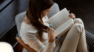 Person reading a book in a living room chair with bright white light from a lamp illuminating the reading area.