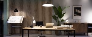 A group of desk and ceiling lamps illuminate a home office workspace with a wooden desk, chair, and architectural drawings.