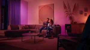 Couple sitting together on a living room couch, illuminated by soft purple and orange smart lighting.