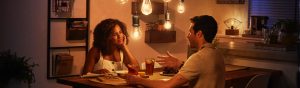 Two people sharing a meal and conversation at a dining table, illuminated by warm pendant smart bulbs in a modern kitchen setting.