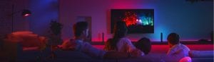 A group of people watching TV in a living room with colorful smart lighting illuminating the walls and furniture.