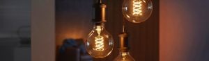 A collection of smart filament bulbs with spiral design, suspended from dark fixtures, emitting warm light onto adjacent walls.