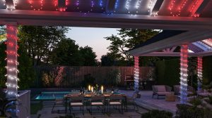 LED party lights for outdoors in red, blue, and white are wrapped around pergola columns and beams, illuminating a patio dining area. 