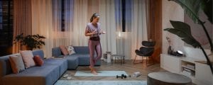 Person in yoga attire adjusting smart lighting in a modern living room, with fitness equipment and soft ambient light on display.