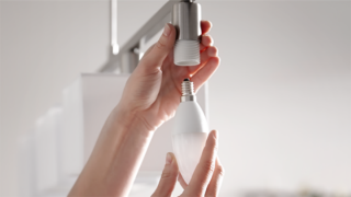 Hands installing a white smart light bulb into a ceiling socket, demonstrating setup of smart lighting solutions.