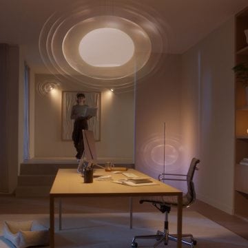 A person stands in a modern home office, illuminated by smart ceiling and wall lights, working with a laptop near a desk.
